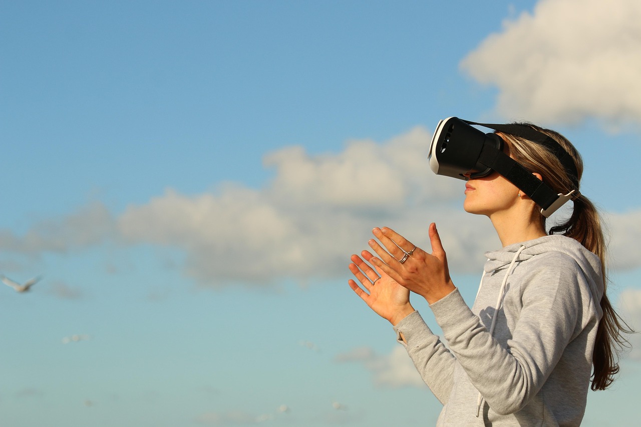 A woman wearing a virtual reality headset outdoors against an open sky