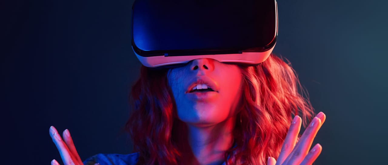 A woman in a VR headset lit by red and blue light, hands raised in front of her